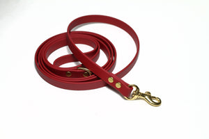 Red faux leather dog leash with gold hardware on a white background