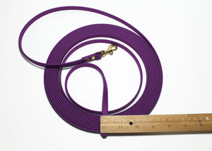 Purple dog leash with a gold clasp on a white background, measured by a wooden ruler.